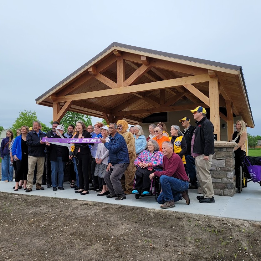 A group of Lions and city officials stand in front of a new picnic shelter holding a ribbon.